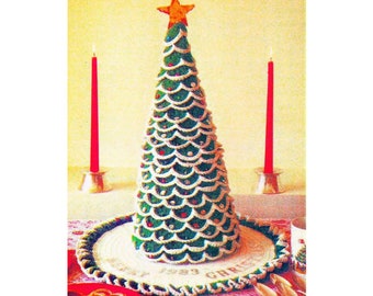 Puede incluir: Un centro de mesa de Navidad de ganchillo en forma de árbol con una estrella en la parte superior, rodeado de una servilleta de ganchillo con el texto "Feliz Navidad". Dos velas rojas están a cada lado del árbol.