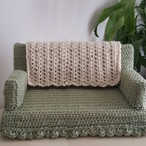 May include: A crocheted green sofa with a white crocheted blanket on top. The sofa has a scalloped edge and is made with a textured stitch.