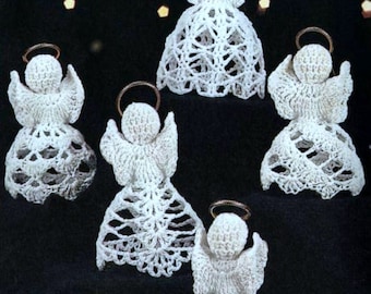 May include: Five white crocheted angel ornaments with gold haloes. The angels are arranged in a circle on a black background.