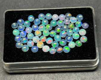 Puede incluir: Una colección de ópalos redondos e iridiscentes, exhibidos en un estuche forrado de terciopelo negro con bordes plateados. Los ópalos exhiben una gama de colores, incluyendo azul, verde y destellos de rojo y amarillo, creando una exhibición vibrante.