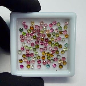 Könnte beinhalten: Eine Sammlung kleiner, runder Edelsteine in verschiedenen Farben, darunter Rosa, Grün, Gelb und Blau. Die Edelsteine befinden sich in einer weißen, quadratischen Kunststoffschale. Die Edelsteine scheinen poliert und facettiert zu sein.
