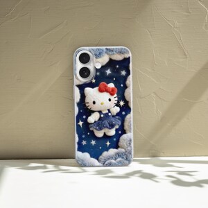 May include: A phone case featuring a 3D Hello Kitty design. The case has a blue starry night background with white clouds and a white Hello Kitty wearing a blue dress and a red bow. The case is designed for a smartphone.