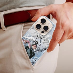 K&ouml;nnte beinhalten: Eine transparente Handyh&uuml;lle mit einer detaillierten Illustration einer Figur in einem Baum mit wei&szlig;en Bl&uuml;ten. Die H&uuml;lle wird in einer Tasche gehalten, mit einem braunen G&uuml;rtel und einer Uhr sichtbar.