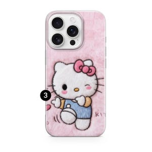 May include: Pink phone case with a fuzzy texture and a Hello Kitty design. The design features a white cat with a pink bow, wearing a blue outfit, and winking. The case has a camera cutout.