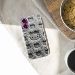 May include: A phone case featuring a repeating pattern of Hello Kitty faces on a gray, fluffy background. The case has a pink camera lens surround. The image also shows a bowl of cereal, a cup of coffee, and a wooden cutting board.