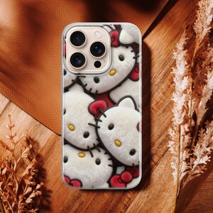 May include: A phone case featuring a repeating pattern of Hello Kitty faces. The case has a clear border and a plush, textured appearance. The background is a mix of brown leather and wood.