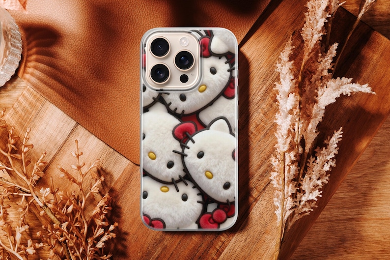 May include: A phone case featuring a repeating pattern of Hello Kitty faces. The case has a clear border and a plush, textured appearance. The background is a mix of brown leather and wood.