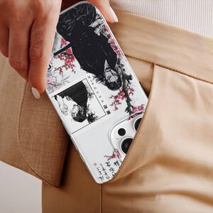 K&ouml;nnte beinhalten: Eine wei&szlig;e Handyh&uuml;lle mit einer Manga-Illustration mit einer schwarzhaarigen Figur, Kirschbl&uuml;ten und japanischem Text. Die H&uuml;lle ist teilweise in einer beigefarbenen Tasche zu sehen.
