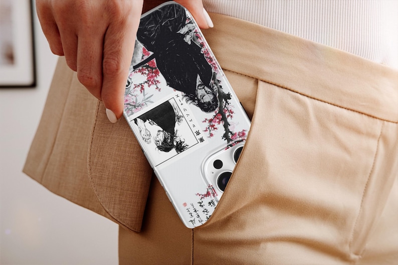 K&ouml;nnte beinhalten: Eine wei&szlig;e Handyh&uuml;lle mit einer Manga-Illustration mit einer schwarzhaarigen Figur, Kirschbl&uuml;ten und japanischem Text. Die H&uuml;lle ist teilweise in einer beigefarbenen Tasche zu sehen.