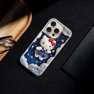 May include: A phone case featuring a Hello Kitty design. The case has a blue background with white clouds and stars. Hello Kitty is wearing a blue dress and a red bow. The case is on a black surface.