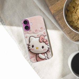 May include: Pink phone case featuring a Hello Kitty design. The case has a light pink background with a repeating pattern of hearts and bows. The Hello Kitty character is in the center, wearing a pink dress and bow. The phone case is on a light-colored surface.
