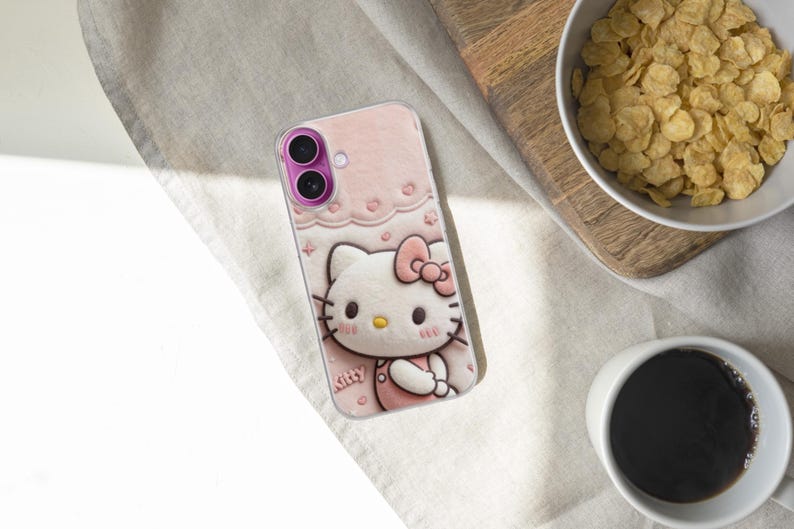May include: Pink phone case featuring a Hello Kitty design. The case has a light pink background with a repeating pattern of hearts and bows. The Hello Kitty character is in the center, wearing a pink dress and bow. The phone case is on a light-colored surface.