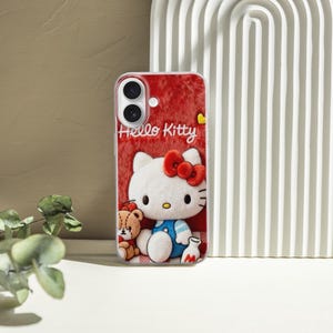 May include: A red phone case featuring Hello Kitty with a red bow, a teddy bear, and the words "Hello Kitty". The case has a textured background and is set against a neutral backdrop.