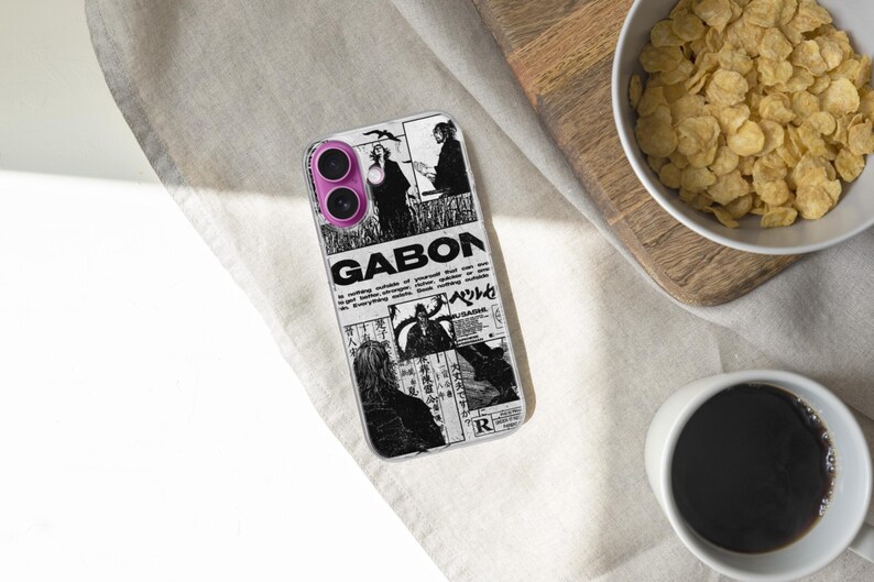 K&ouml;nnte beinhalten: Eine transparente Handyh&uuml;lle mit einem schwarz-wei&szlig;en Grafikdesign mit dem Wort "GABON" und anderem Text. Die H&uuml;lle liegt auf einer wei&szlig;en Oberfl&auml;che, neben einer Sch&uuml;ssel mit M&uuml;sli und einer Tasse Kaffee.