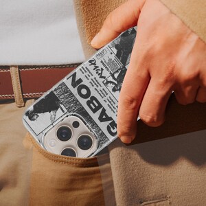 K&ouml;nnte beinhalten: Schwarz-wei&szlig;es Handycase mit Zeitungsdesign und dem Wort "GABON". Das Case befindet sich in einer Tasche, mit einem braunen G&uuml;rtel und einer beigen Hose im Hintergrund.