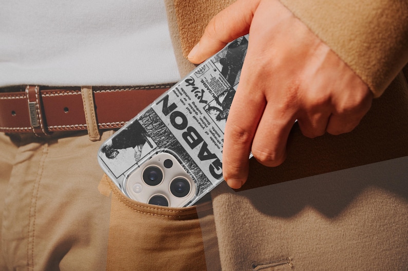 K&ouml;nnte beinhalten: Schwarz-wei&szlig;es Handycase mit Zeitungsdesign und dem Wort "GABON". Das Case befindet sich in einer Tasche, mit einem braunen G&uuml;rtel und einer beigen Hose im Hintergrund.