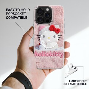 May include: Pink phone case with a Hello Kitty design. The case has a fluffy texture and features a white Hello Kitty character with a red bow. The text "hellokitty" is displayed in pink. The case is labeled "EASY TO HOLD POPSOCKET COMPATIBLE" and "LIGHT WEIGHT SOFT AND FLEXIBLE".