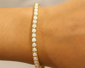 May include: A gold-toned bracelet featuring a row of white opal gemstones. The bracelet is worn on a wrist, showcasing the delicate design and the play of light on the opals. The bracelet is a piece of jewelry.