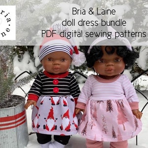 Pode incluir: Duas bonecas vestindo vestidos com padrões diferentes. A boneca à esquerda está vestindo uma camisa de manga comprida listrada de preto e branco com um botão vermelho e um vestido branco com um padrão de gnomo. A boneca à direita está vestindo uma camisa de manga comprida listrada de rosa e branco e um vestido rosa com um padrão de árvore. Ambas as bonecas estão vestindo leggings pretos e meias brancas. As bonecas estão em pé na neve. O texto "Bria & Laine doll dress bundle PDF digital sewing patterns" está no topo da imagem.