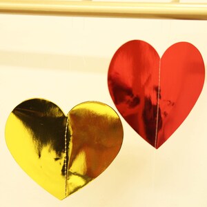 Peut inclure: Deux décorations en forme de cœur, une dorée et une rouge, avec une finition métallique brillante. Elles sont suspendues à une tige en bois, suggérant un thème festif ou décoratif.