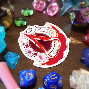 Könnte beinhalten: Ein Aufkleber mit einem rot-weißen, stilisierten Design mit geometrischen Formen und einem zentralen Emblem. Der Aufkleber ist von verschiedenen bunten Würfeln und Glasperlen umgeben, was auf ein Tabletop-Gaming-Thema hindeutet.