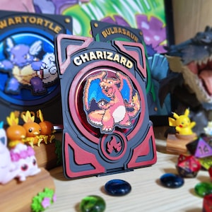 May include: A Charizard-themed display case with a pixelated image of Charizard. The case is red, black, and gray, with the name "CHARIZARD" in gold lettering. Other Pokemon-themed items are in the background.