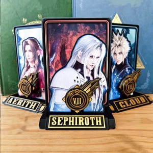 May include: Three rectangular display stands featuring character portraits from Final Fantasy VII. The centre stand depicts Sephiroth, while the side stands feature Aerith and Cloud. Each stand includes a gold VII emblem and a nameplate.