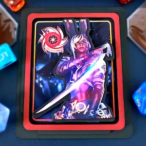 May include: A fantasy card with a character holding a glowing sword and rabbit ears. The card has a red border and is set against a dark background. Various coloured dice surround the card, suggesting a tabletop game.