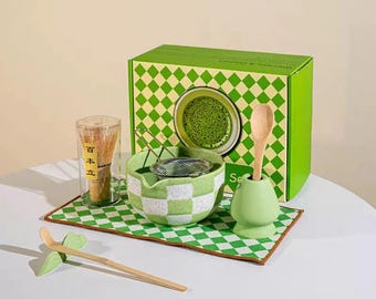 May include: A matcha tea set with a green and white checkered bowl, a bamboo whisk, a wooden spoon, and a green ceramic spoon holder. The set includes a green box with a matcha tea image and a green and white checkered pattern.