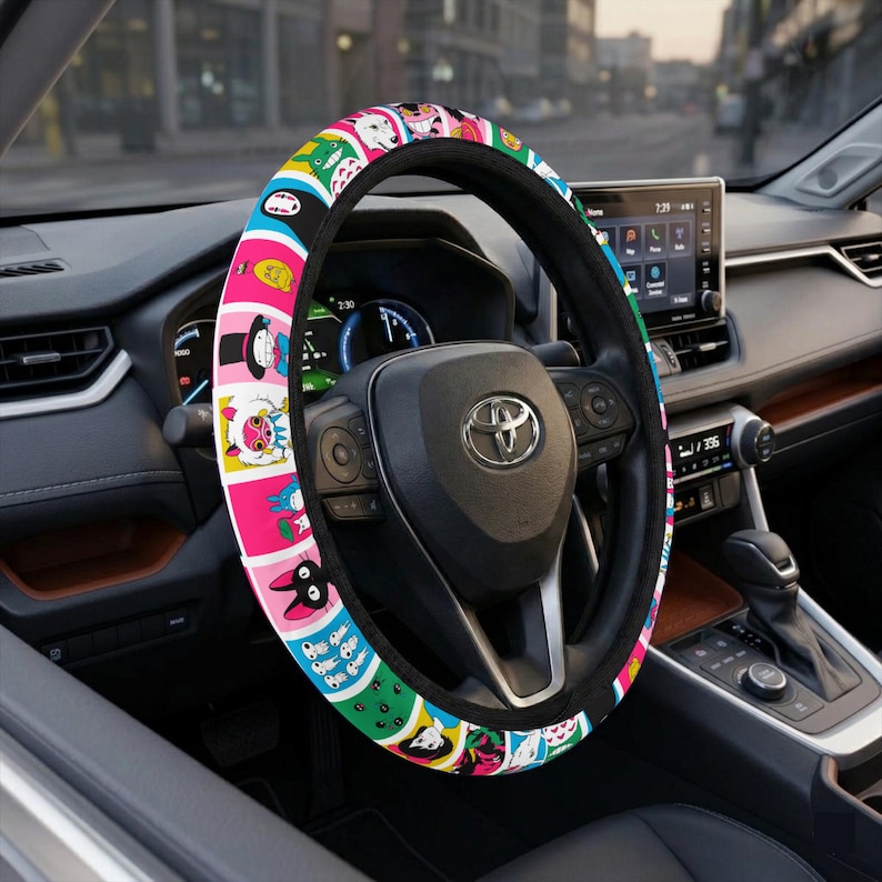 May include: A steering wheel cover featuring a vibrant, multi-colored grid pattern of various cartoon character illustrations. The cover is installed on a black steering wheel with a central Toyota logo, set within a modern vehicle interior dashboard.