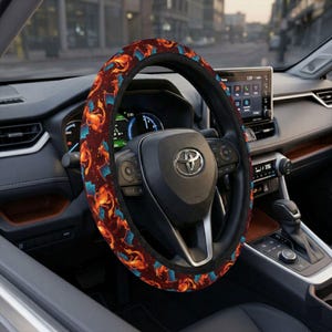 Puede incluir: Una funda para volante de coche con un patrón repetido de dragones naranjas y azules sobre un fondo rojo oscuro. El volante es negro y está dentro de un coche.
