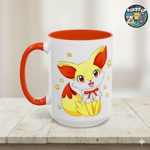 May include: White ceramic mug with a red interior and handle. The mug features a cartoon Fennekin character with yellow and red fur, surrounded by yellow stars. A Poketop logo is visible on the top right.