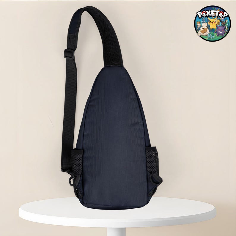 May include: Navy blue sling bag with a black adjustable strap and a black mesh pocket on each side. The bag has a rounded shape and a black padded shoulder strap. A circular logo with cartoon characters is visible in the upper right corner.