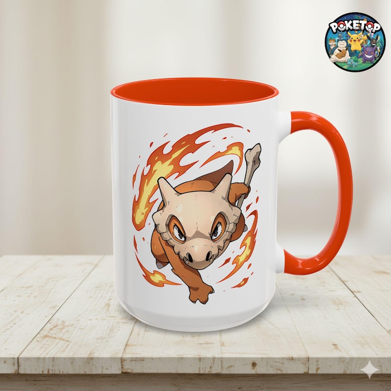 May include: White ceramic mug with an orange interior and handle. The mug features a cartoon illustration of a Cubone character surrounded by flames. A Poketop logo is visible on the top right.