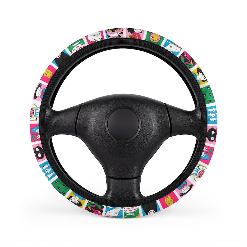 May include: A black steering wheel cover featuring a repeating pattern of colorful square tiles. Each tile displays a different cartoon character illustration in various colors including pink, green, blue, and yellow against a white background.