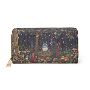 May include: A long, zipped wallet featuring a whimsical forest scene with a large, round, blue creature, mushrooms, and a fox. The wallet has a gold-coloured zip and pull.