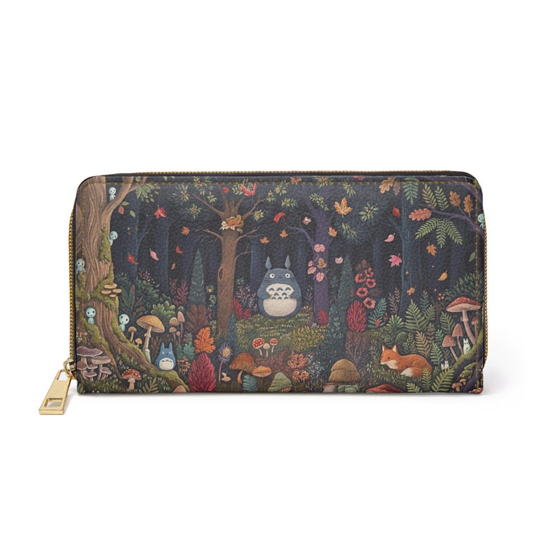 May include: A long, zipped wallet featuring a whimsical forest scene with a large, round, blue creature, mushrooms, and a fox. The wallet has a gold-coloured zip and pull.