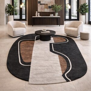 May include: An oval area rug with a geometric design in black, brown, and cream colors. The rug is placed in a modern living space with two cream-colored armchairs and a dark brown coffee table.