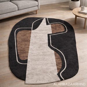 May include: An oval area rug with a modern geometric design. The rug features a black border with a central pattern of beige, brown, and white shapes. The rug is placed on a hardwood floor.