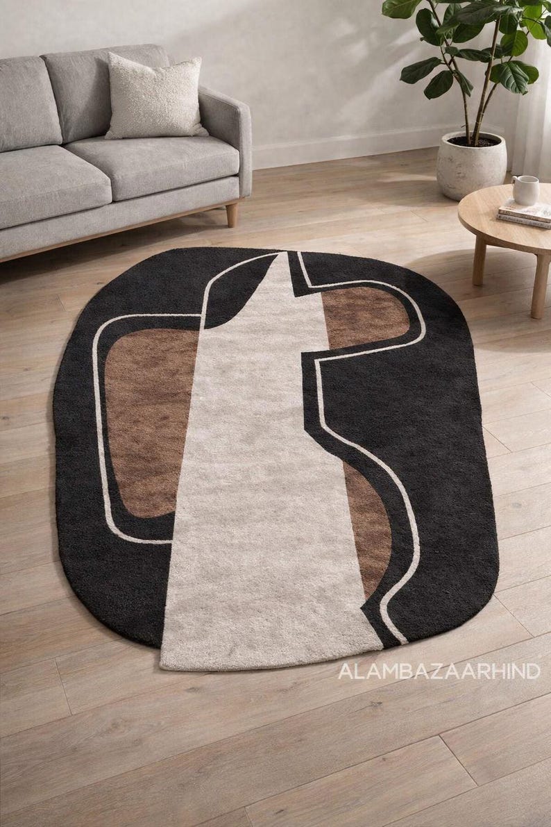 May include: An oval area rug with a modern geometric design. The rug features a black border with a central pattern of beige, brown, and white shapes. The rug is placed on a hardwood floor.