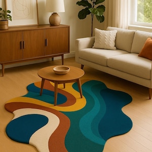 May include: A colorful, abstract area rug with a wavy design in shades of blue, teal, yellow, brown, and cream. The rug is placed on a hardwood floor in a living room setting. The text "ALAMBAZAAR HIND" is at the bottom.