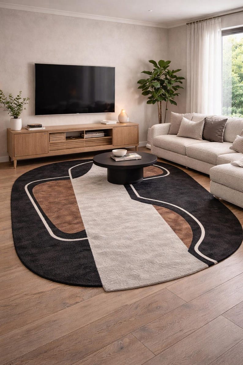 May include: An oval area rug with a modern design. The rug features a black background with brown and beige geometric shapes outlined in white. The rug is placed in a living room with a sofa, TV, and coffee table.