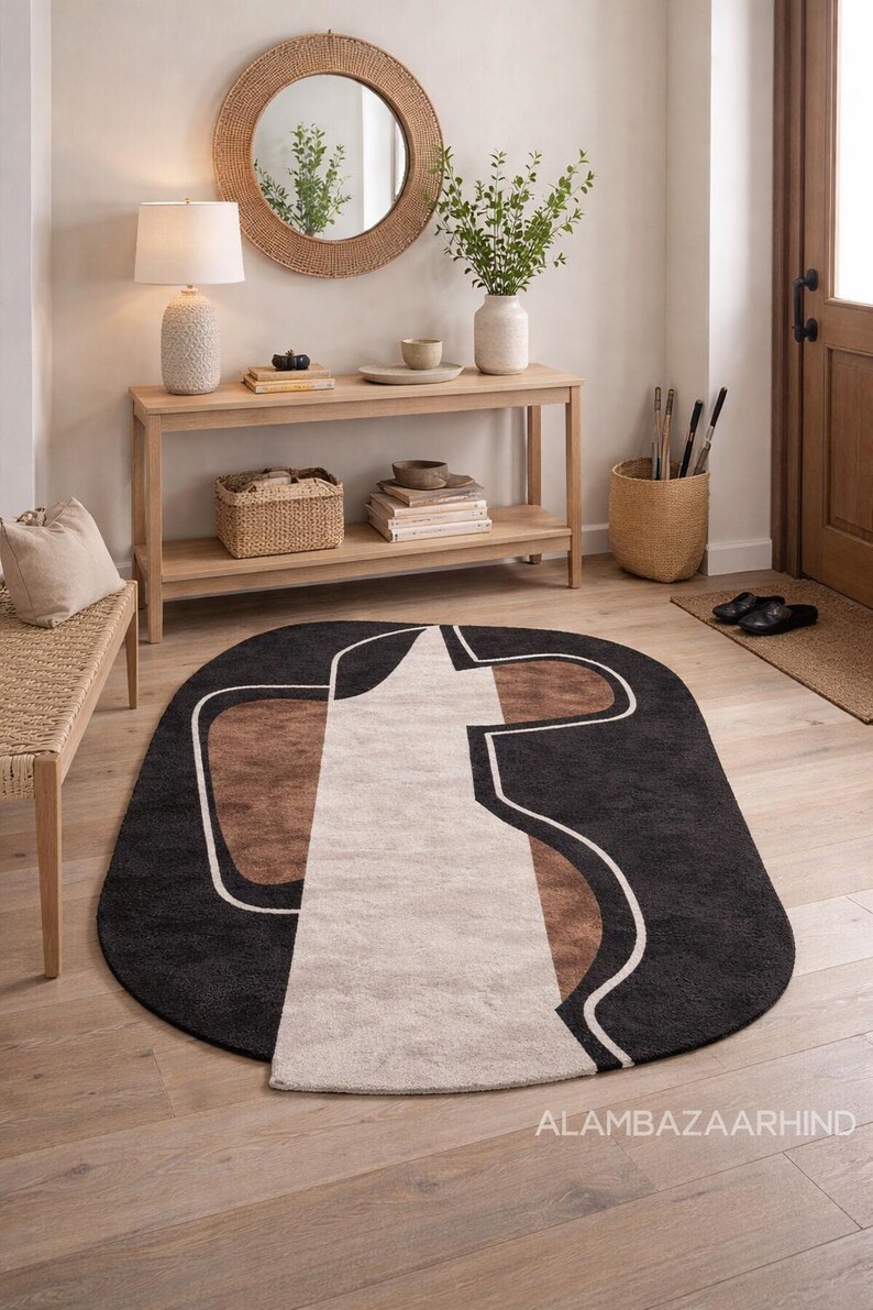 May include: Oval area rug with a modern design. The rug features a black background with a white, brown, and beige geometric pattern. The rug is placed on a hardwood floor in a well-lit entryway.