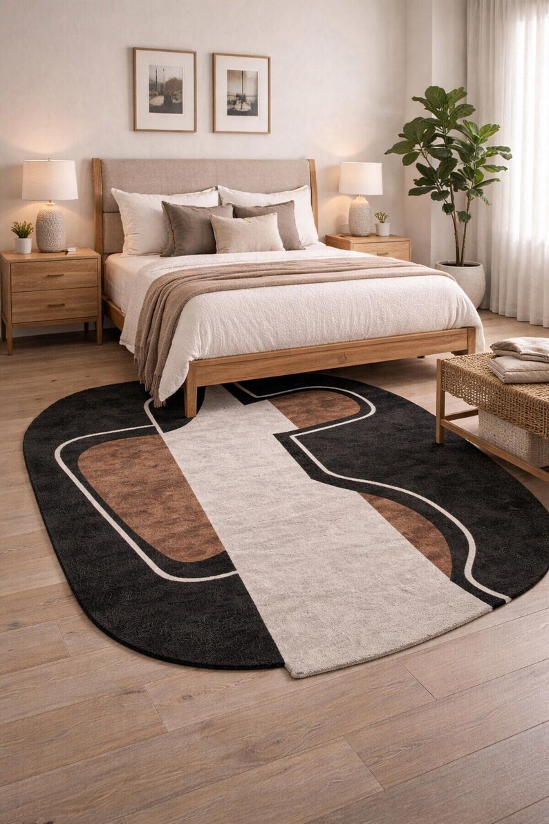 May include: An oval area rug with a modern design. The rug features a black background with geometric shapes in brown and off-white, outlined with a white border. The rug is placed in a bedroom setting.