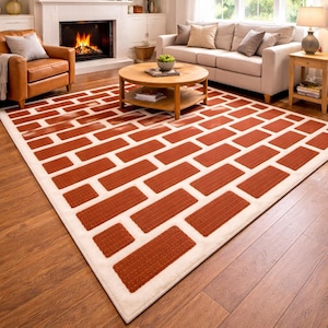 May include: A rectangular area rug with a brick pattern in shades of red-orange and white. The rug is placed on a hardwood floor in a living room setting, with a fireplace and furniture visible in the background.
