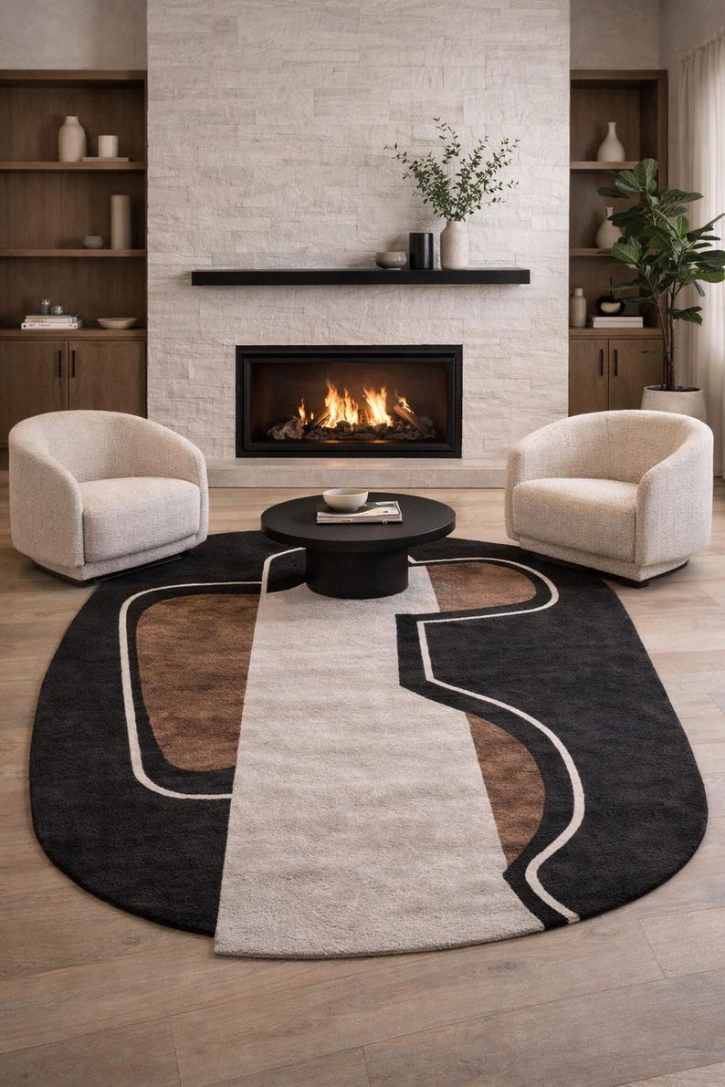 May include: An oval area rug with a geometric design in black, brown, and cream colors. The rug is placed in front of a fireplace with two cream-colored armchairs and a black coffee table.