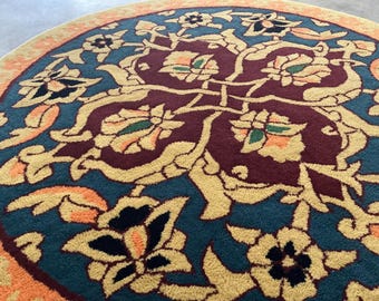 May include: A round rug with an intricate floral design. The rug features a teal background with a burgundy center and gold and orange floral patterns. The border is a light orange color. The rug's design is symmetrical and detailed.