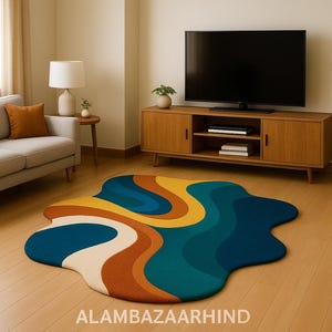 May include: A colorful, abstract area rug with a wavy design in shades of blue, yellow, orange, and cream. The rug is placed on a hardwood floor in a living room setting, with a sofa, TV, and wooden cabinet visible.