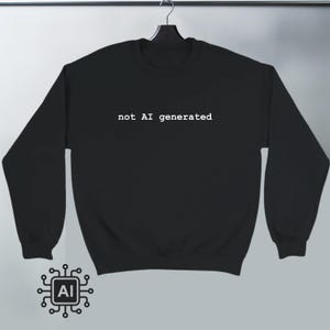 Puede incluir: Sudadera negra con el texto blanco "not AI generated". La sudadera está colgada de una percha negra. Un gráfico de una placa de circuito con las letras "AI" está en la esquina inferior izquierda.