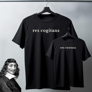 May include: Two black t-shirts hanging on a rack. The larger shirt has the text "res cogitans" in white, and the smaller shirt has "res extensa". A portrait of René Descartes is in the lower left corner.